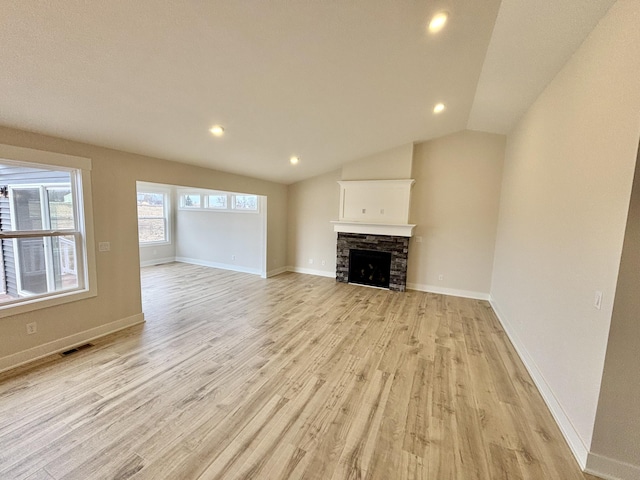 unfurnished living room with baseboards, visible vents, vaulted ceiling, light wood-style floors, and a fireplace