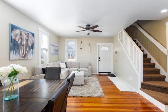 living area featuring baseboards, wood finished floors, stairway, and a ceiling fan