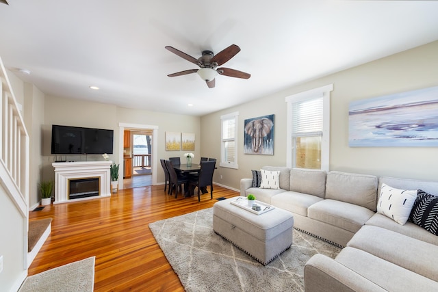 living area with a wealth of natural light, wood finished floors, ceiling fan, and baseboards