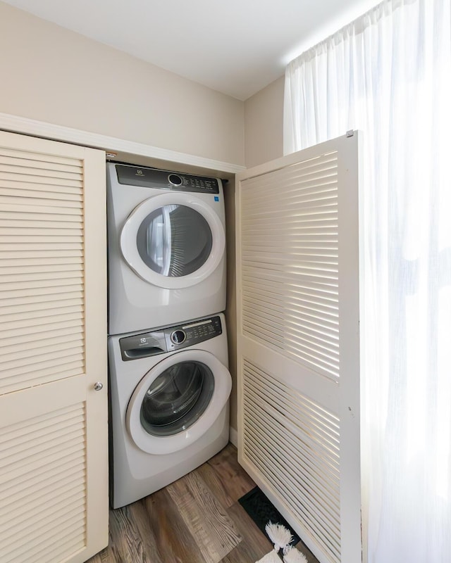 washroom featuring wood finished floors, stacked washer / drying machine, and laundry area