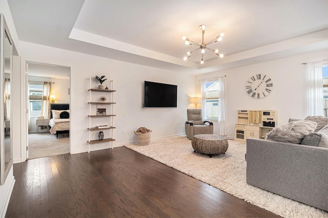 living room featuring a raised ceiling, wood-type flooring, and an inviting chandelier