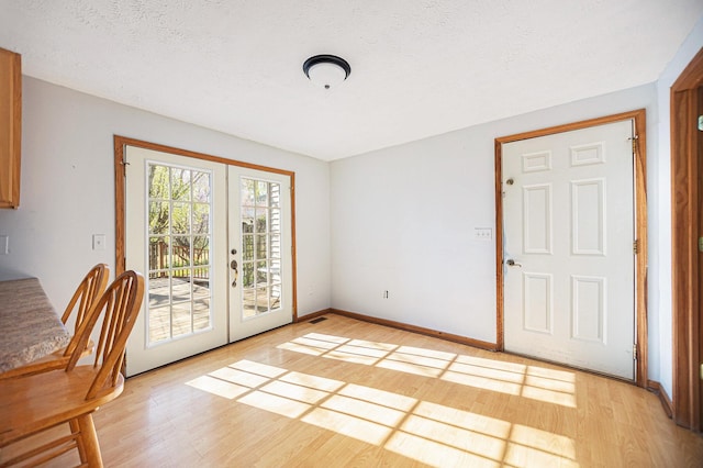 unfurnished dining area with light wood-type flooring, a textured ceiling, and french doors