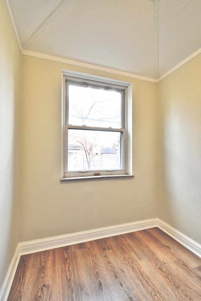 empty room with hardwood / wood-style flooring, vaulted ceiling, and ornamental molding