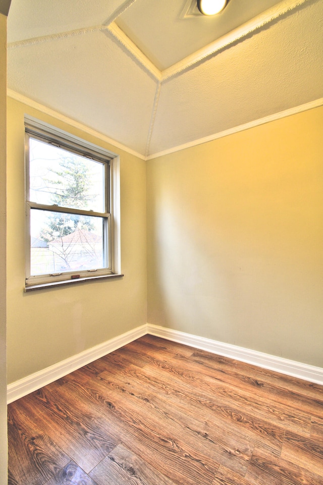 unfurnished room with wood-type flooring, vaulted ceiling, and ornamental molding