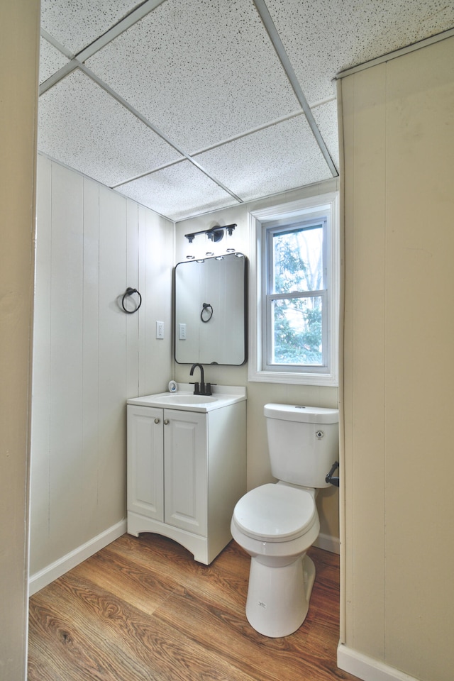 bathroom with hardwood / wood-style floors, vanity, toilet, and a drop ceiling