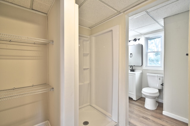 bathroom featuring a drop ceiling, a shower, sink, hardwood / wood-style flooring, and toilet