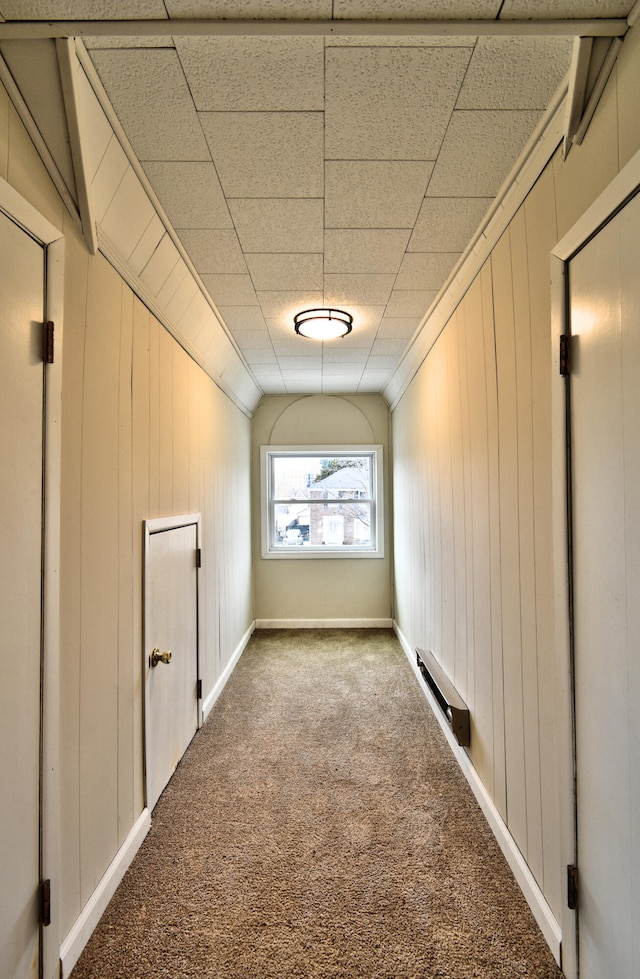 hall featuring carpet, vaulted ceiling, baseboard heating, and wooden walls