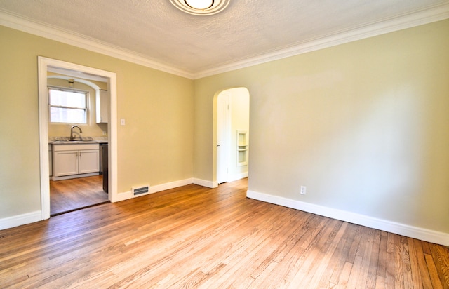 empty room with a textured ceiling, light hardwood / wood-style floors, ornamental molding, and sink