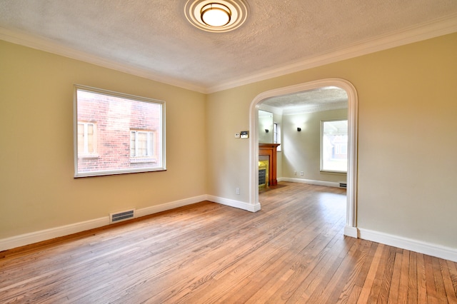 spare room featuring plenty of natural light, light hardwood / wood-style floors, ornamental molding, and a textured ceiling