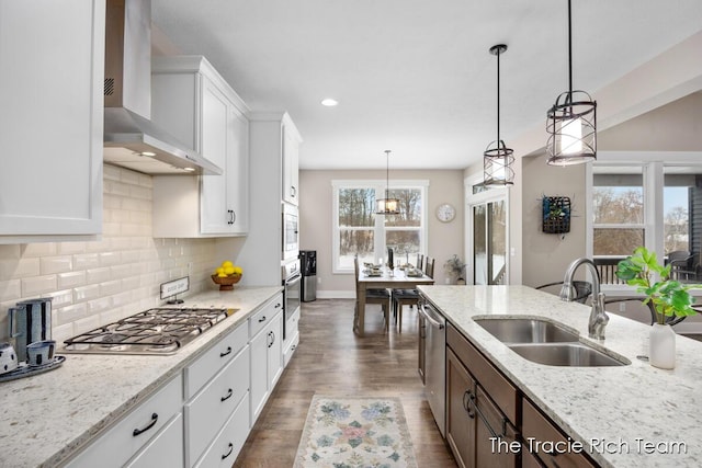 kitchen with sink, wall chimney range hood, white cabinets, and decorative light fixtures