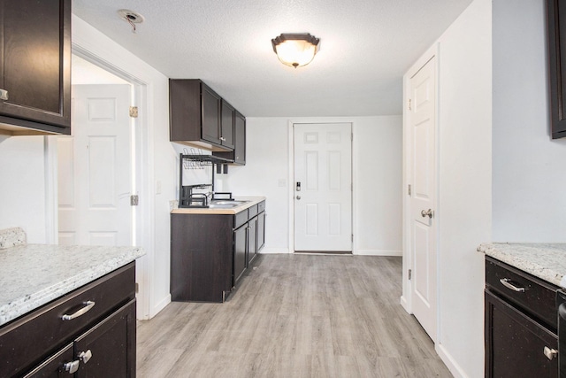 kitchen with dark brown cabinets, light stone counters, light hardwood / wood-style flooring, and a textured ceiling