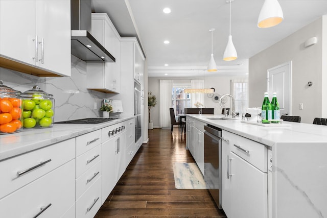 kitchen featuring sink, hanging light fixtures, stainless steel dishwasher, wall chimney exhaust hood, and white cabinetry