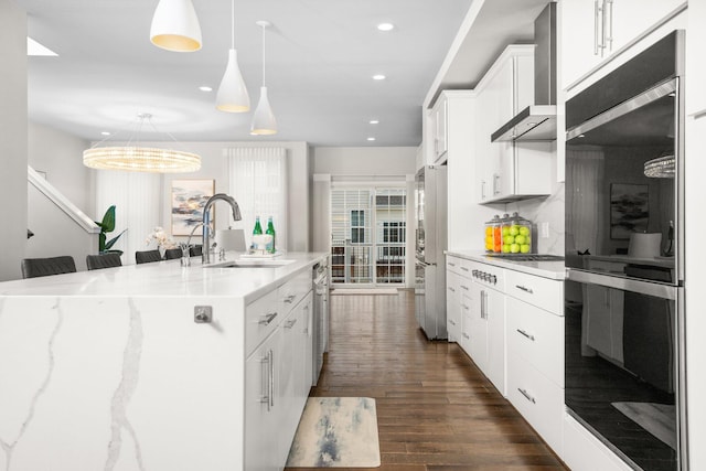 kitchen with a kitchen island with sink, white cabinets, sink, wall chimney exhaust hood, and appliances with stainless steel finishes