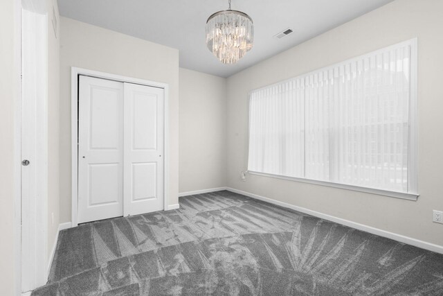 unfurnished bedroom with a closet, a chandelier, and dark carpet