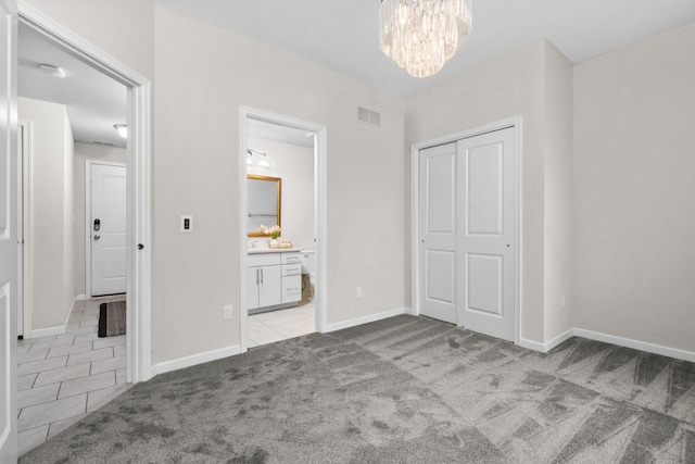 unfurnished bedroom with light colored carpet, ensuite bath, a closet, and a notable chandelier