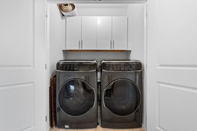 clothes washing area with washing machine and clothes dryer, light tile patterned floors, and cabinets