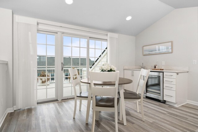 dining space with vaulted ceiling, light hardwood / wood-style floors, wine cooler, and bar