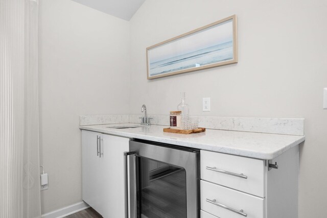 bar featuring wine cooler, light stone countertops, sink, and dark wood-type flooring