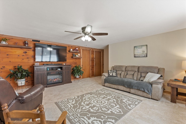 carpeted living room featuring wood walls, ceiling fan, and a fireplace