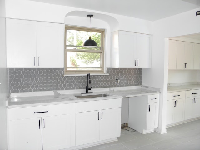 kitchen with tasteful backsplash, white cabinetry, sink, and decorative light fixtures