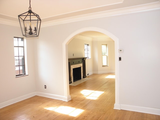 unfurnished living room featuring a premium fireplace, ornamental molding, light hardwood / wood-style floors, and a notable chandelier