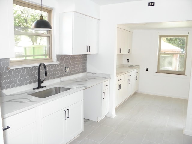 kitchen with white cabinets, sink, decorative backsplash, light stone countertops, and decorative light fixtures