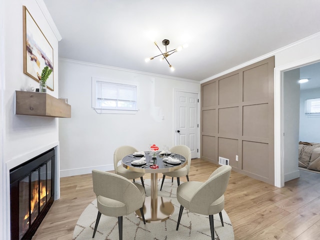 dining room with an inviting chandelier, ornamental molding, and light hardwood / wood-style flooring