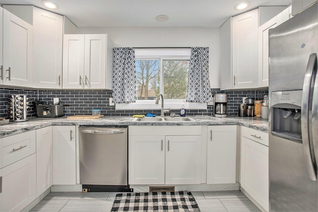 kitchen with appliances with stainless steel finishes, light stone countertops, sink, and white cabinets