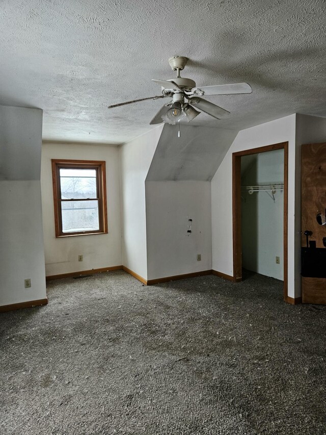 bonus room featuring a textured ceiling, dark carpet, ceiling fan, and lofted ceiling