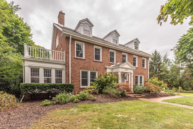 colonial-style house featuring a balcony and a front lawn