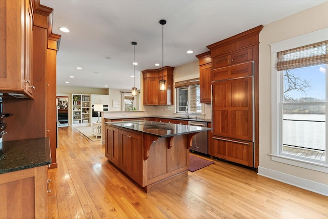 kitchen with a kitchen bar, stainless steel dishwasher, dark stone counters, sink, and pendant lighting