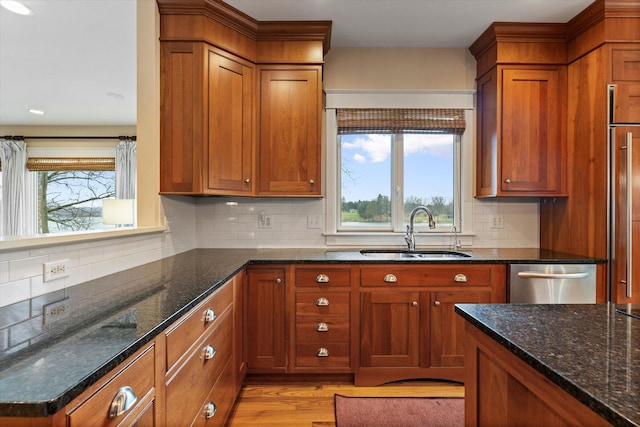 kitchen featuring dark stone counters, sink, light hardwood / wood-style flooring, stainless steel dishwasher, and decorative backsplash