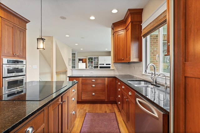 kitchen with pendant lighting, dark stone counters, sink, light wood-type flooring, and stainless steel appliances