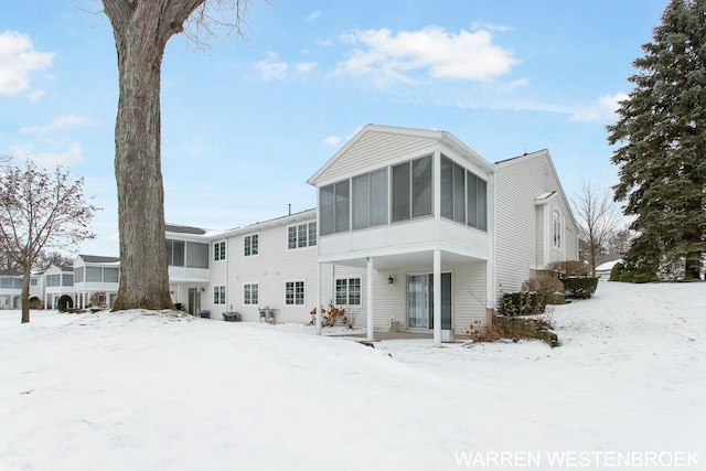 snow covered back of property with a sunroom