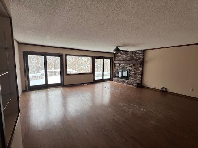 unfurnished living room with ceiling fan, hardwood / wood-style floors, a textured ceiling, and a brick fireplace