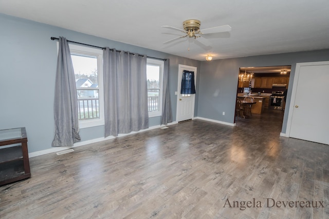 unfurnished living room with ceiling fan with notable chandelier and dark wood-type flooring