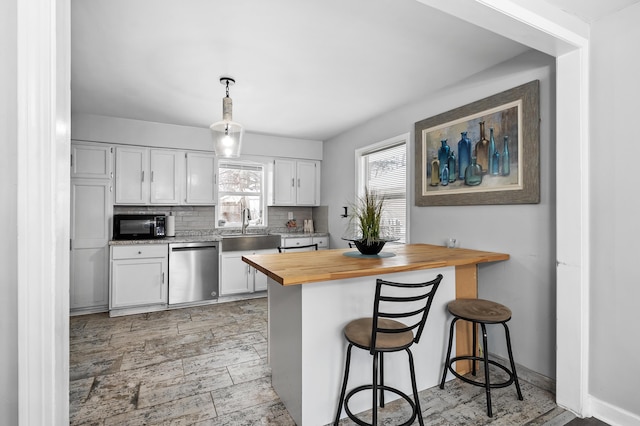 kitchen with backsplash, white cabinets, hanging light fixtures, stainless steel dishwasher, and butcher block counters