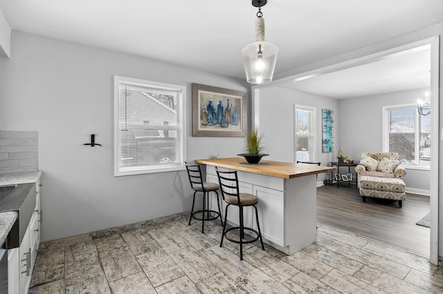 kitchen with kitchen peninsula, a kitchen breakfast bar, decorative light fixtures, butcher block countertops, and white cabinetry