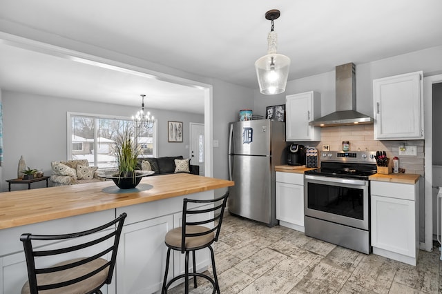 kitchen featuring stainless steel appliances, wall chimney range hood, pendant lighting, butcher block countertops, and white cabinetry