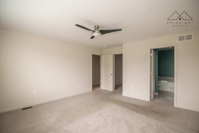 unfurnished bedroom with light carpet, a walk in closet, ceiling fan, connected bathroom, and a closet