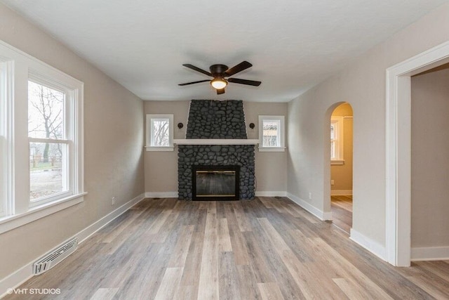 unfurnished living room with light hardwood / wood-style floors, a stone fireplace, ceiling fan, and a healthy amount of sunlight