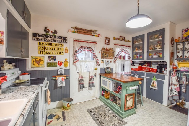 kitchen with wooden walls, sink, electric stove, pendant lighting, and butcher block countertops