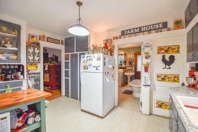 kitchen with white refrigerator, sink, hanging light fixtures, light stone counters, and washer / dryer