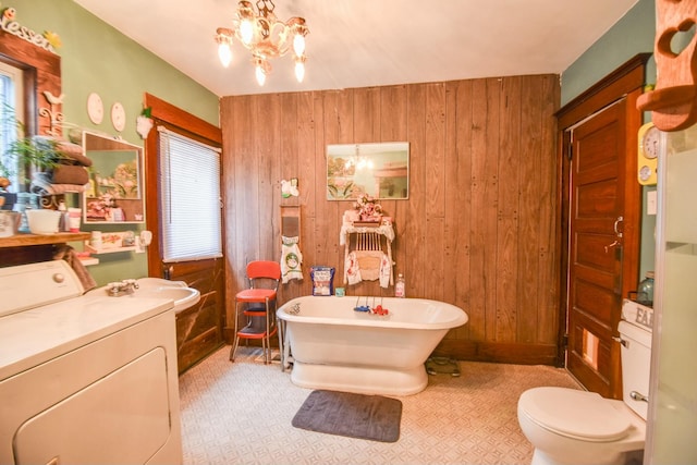 bathroom featuring an inviting chandelier, a bath, washer / clothes dryer, wooden walls, and vanity