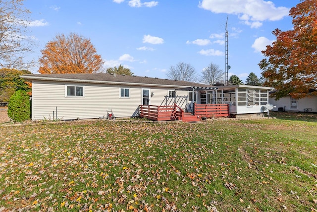 back of property with a sunroom, a wooden deck, and a lawn