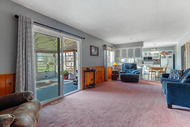 living room featuring wood walls, carpet floors, a textured ceiling, and an inviting chandelier