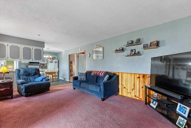 living room with carpet flooring, a textured ceiling, a chandelier, and wooden walls