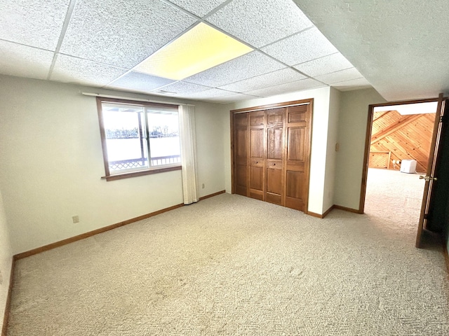 unfurnished bedroom with a paneled ceiling, a closet, wood walls, and carpet flooring