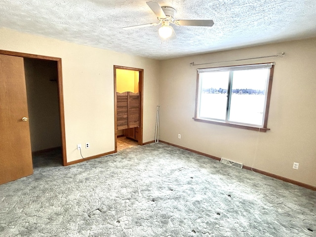 unfurnished bedroom featuring a spacious closet, a textured ceiling, a closet, ceiling fan, and light colored carpet