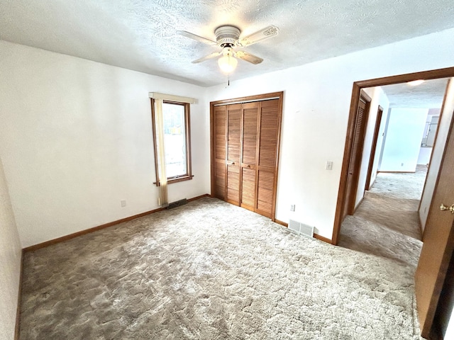 unfurnished bedroom with ceiling fan, a closet, a textured ceiling, and dark colored carpet